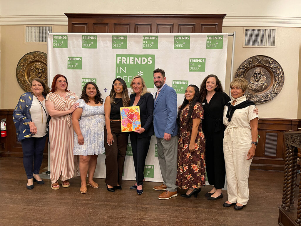 Photo of Rabbi Joshua Levine Grater, Supervisor Barger, Lindsey Reed, Jane Armbruster, Jenny Juarez, and TWR Guests in front the Friends In Deed step-and-repeat at EmpowerHER: Flowers and Flourish