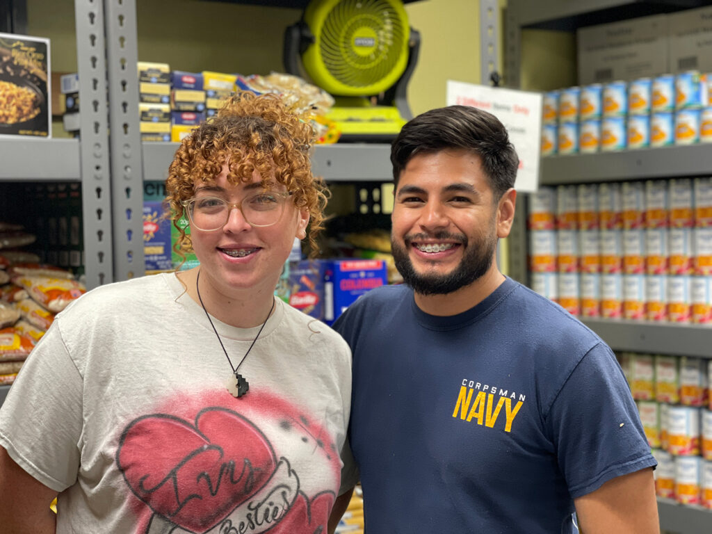 Photo of Ivy and Waldo standing in front of stocked shelves at the Food Pantry.